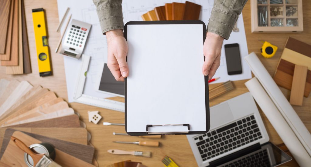 Hands holding clipboard above remodeling supplies