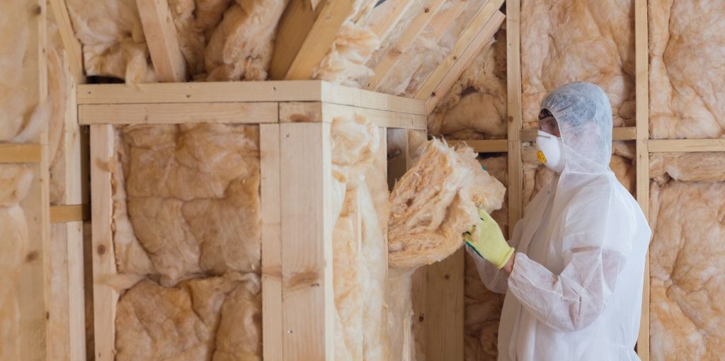 Worker in protective gear holding insulation near exposed wall
