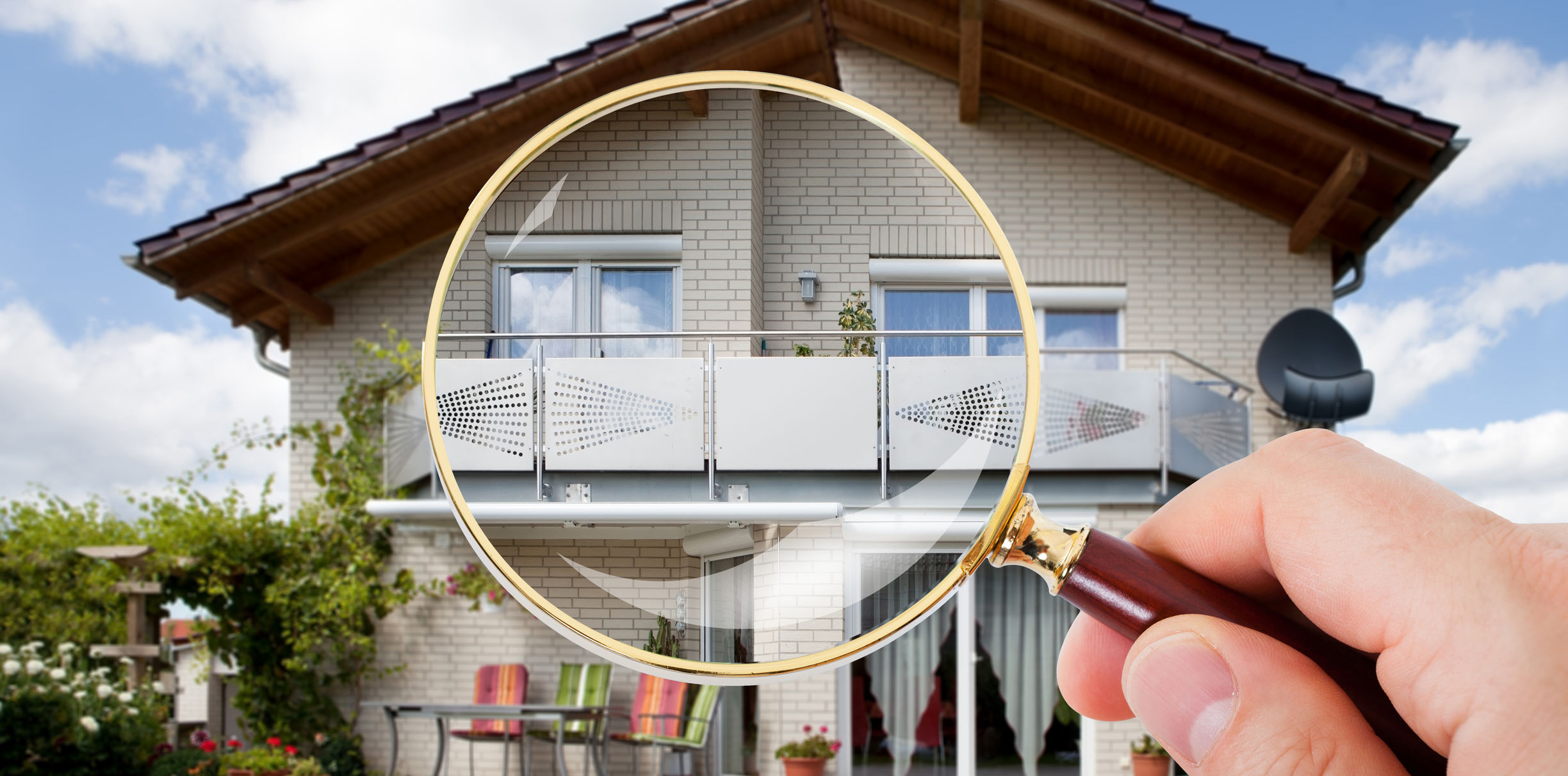 Hand holding magnifying glass in front of house