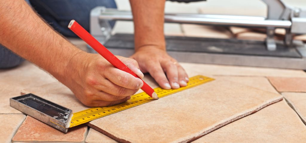 Laying ceramic floor tiles - man hands marking tile to be cut