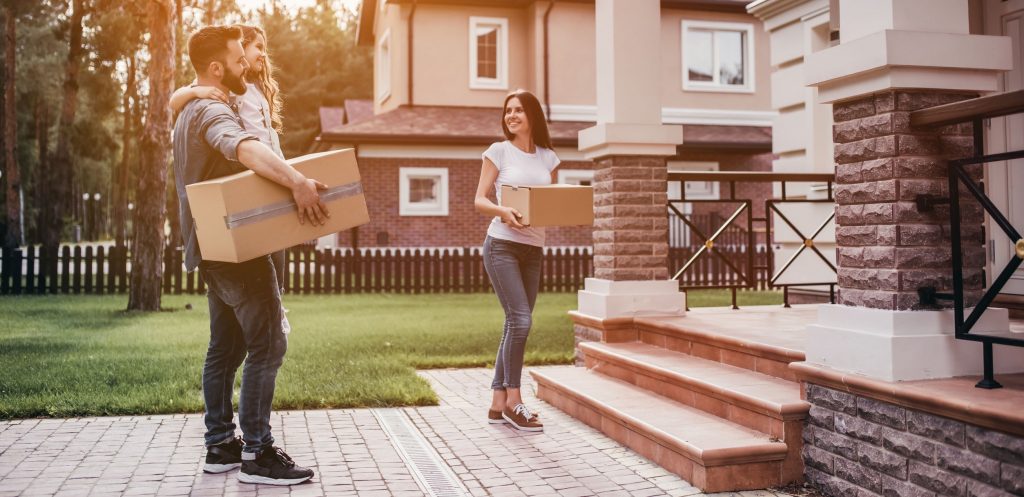 Couple standing near new house with cardboard boxes