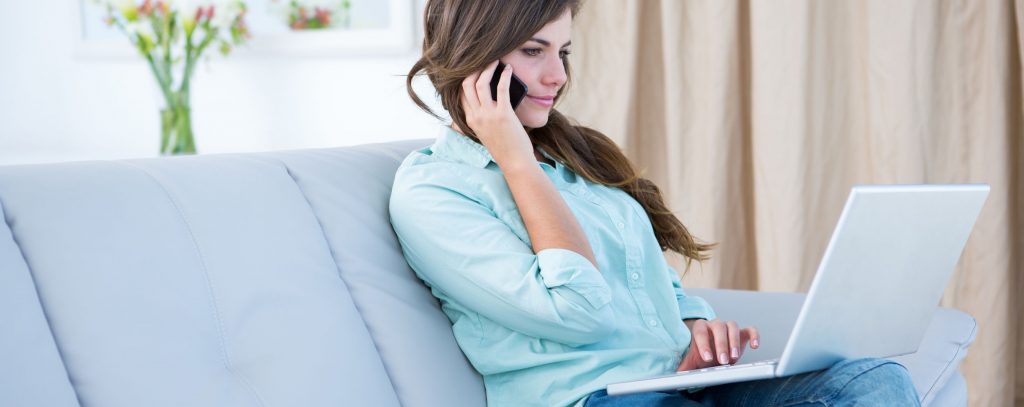 Woman on the phone using her laptop at home in the living room