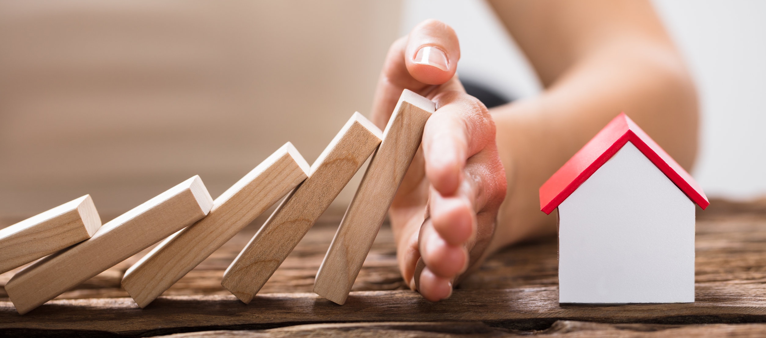 Close-up Of A Human Hand Stopping The Wooden Blocks From Falling On House Model