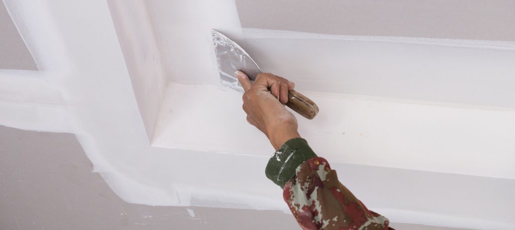 Hand of worker using gypsum plaster ceiling joints at construction site