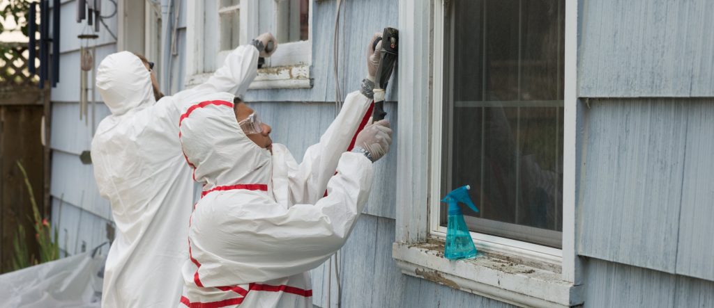 Two house painters in hazmat suits removing lead paint from an old house