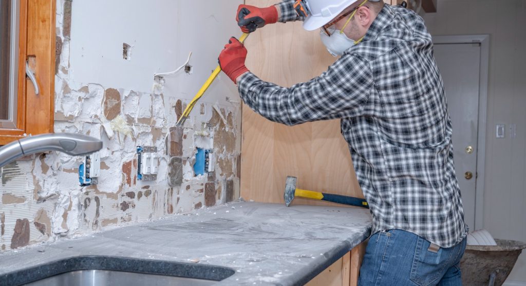 A renovation worker removing kitchen wall tile during a home improvement project