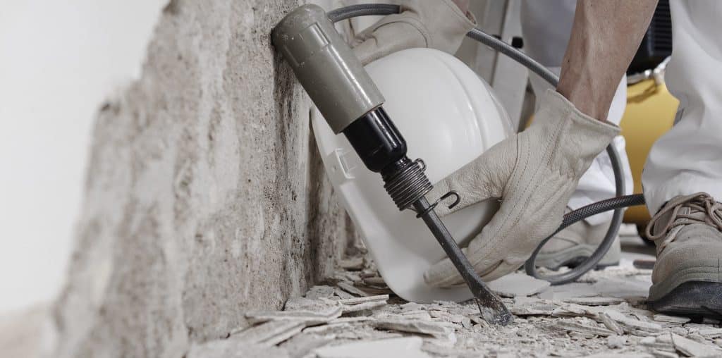 Construction worker with gloves placing helmet near compressor and pneumatic air hammer chisel