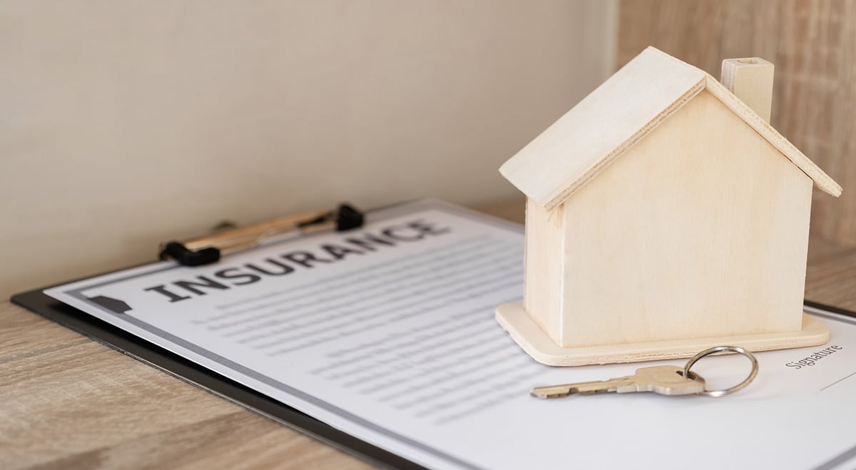 Small wooden model home and key on top of a homeowners insurance form