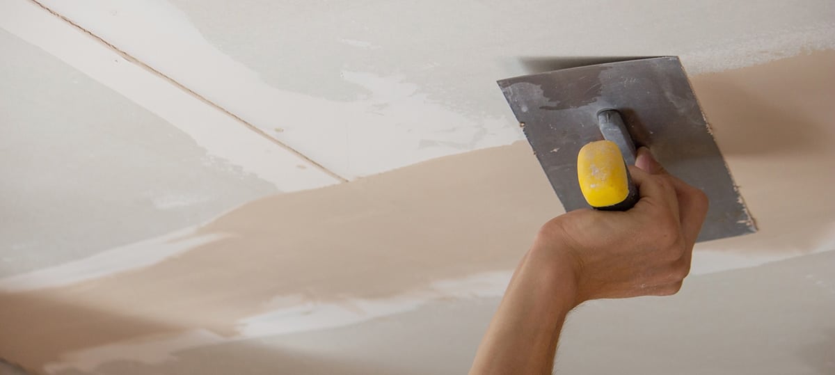 Worker smoothing putty into joints of plasterboard on ceiling